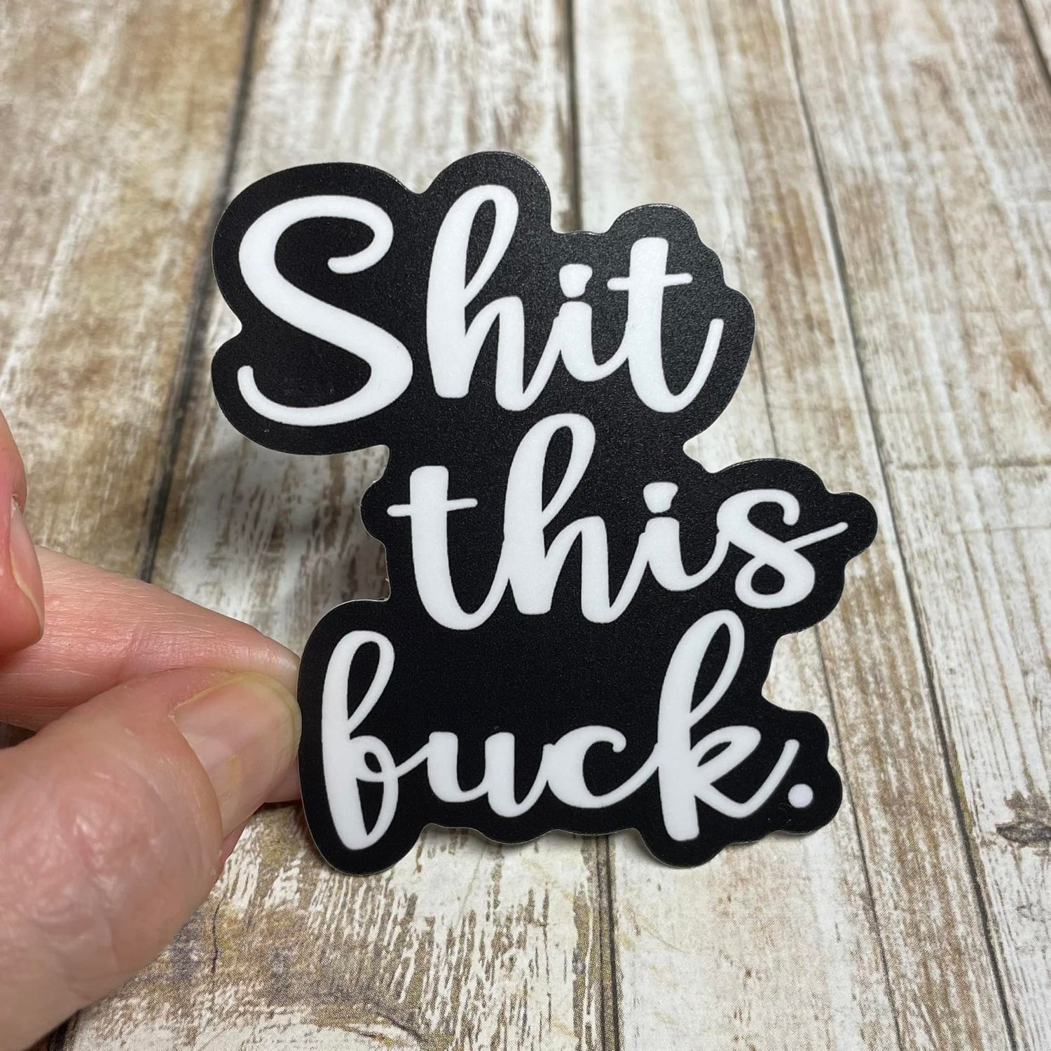 A photo of a vinyl sweary sticker. Its text which reads 'Shit This Fuck.'