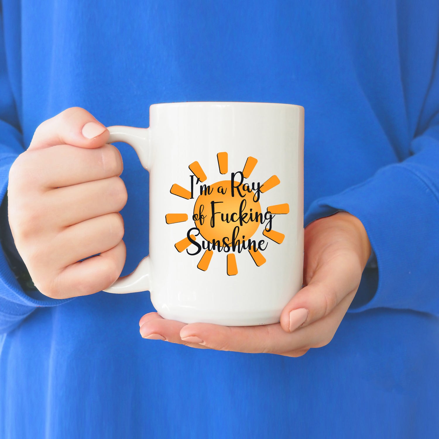 A photo of a funny mug. It's white and has a bright yellow sunshine on it. Text reads, 'I'm a Ray of Fucking Sunshine.'