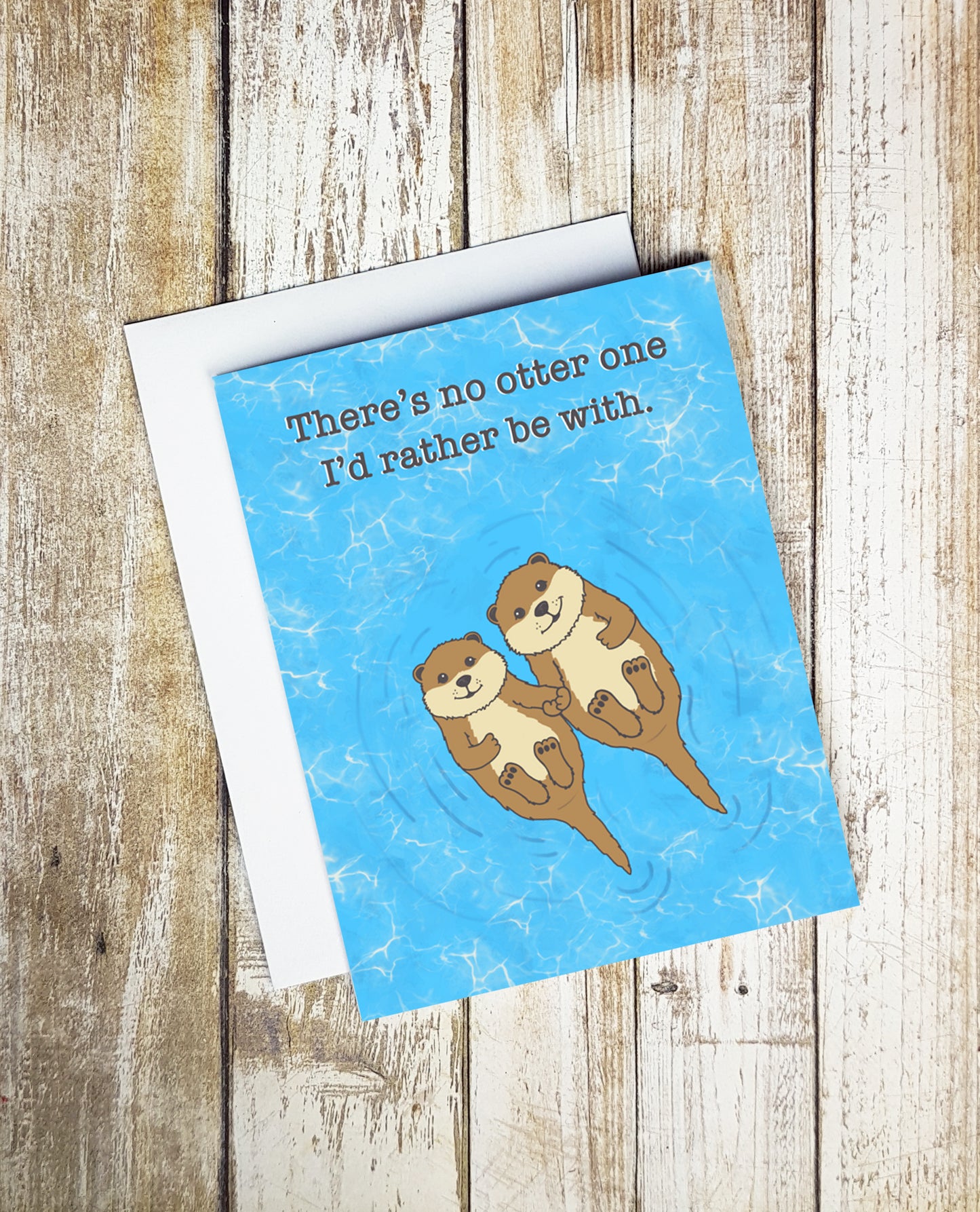 A photo of a blue otter card. It has two otters on it holding paws. Text reads, 'There's no otter one I'd rather be with.'
