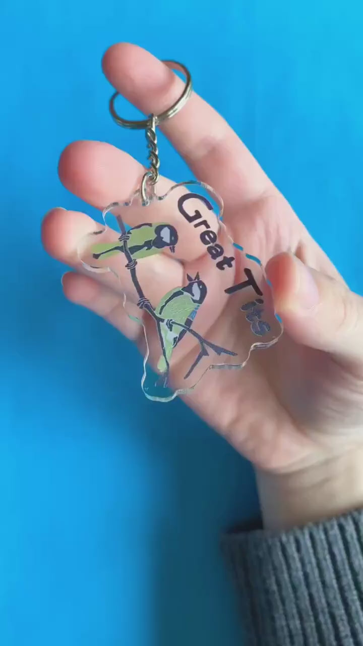 A video of a hand holding up a key chain. It has two blue tits on it. Text on keychain reads 'Great Tits.'