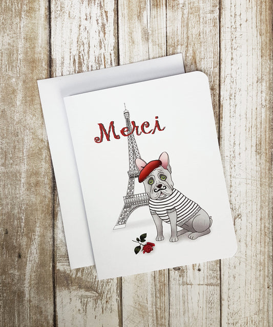 A photo of a thank you card. It has a cartoon Frenchie dog on it. It's sat in front of the Eiffel Tower. It's wearing a beret and has a twirly moustache. Text reads, 'Merci.'