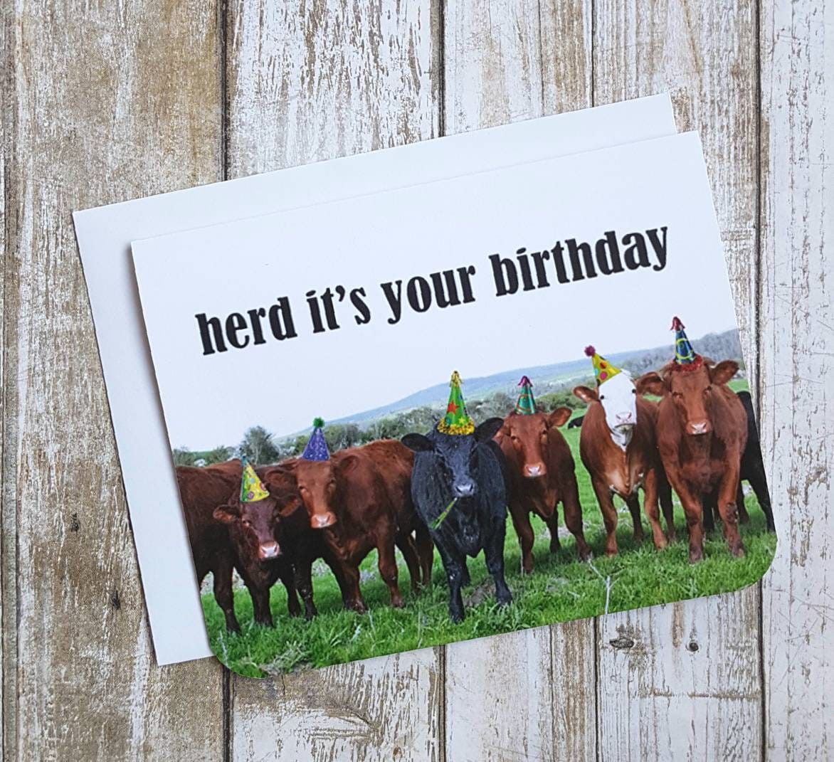 A photo of a birthday card. It has a photo of a herd of cows wearing party hats. Text on card reads, 'herd it's your birthday.'