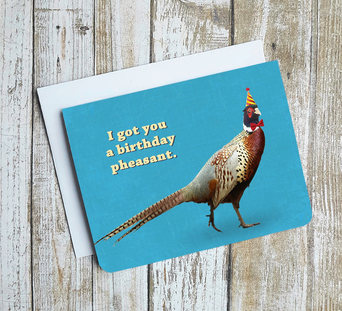 A photo of a blue birthday card. It has a photo of a strutting pheasant on it. It's wearing a bow tie and a party had. Text on card reads, 'I got you a birthday pheasant.'
