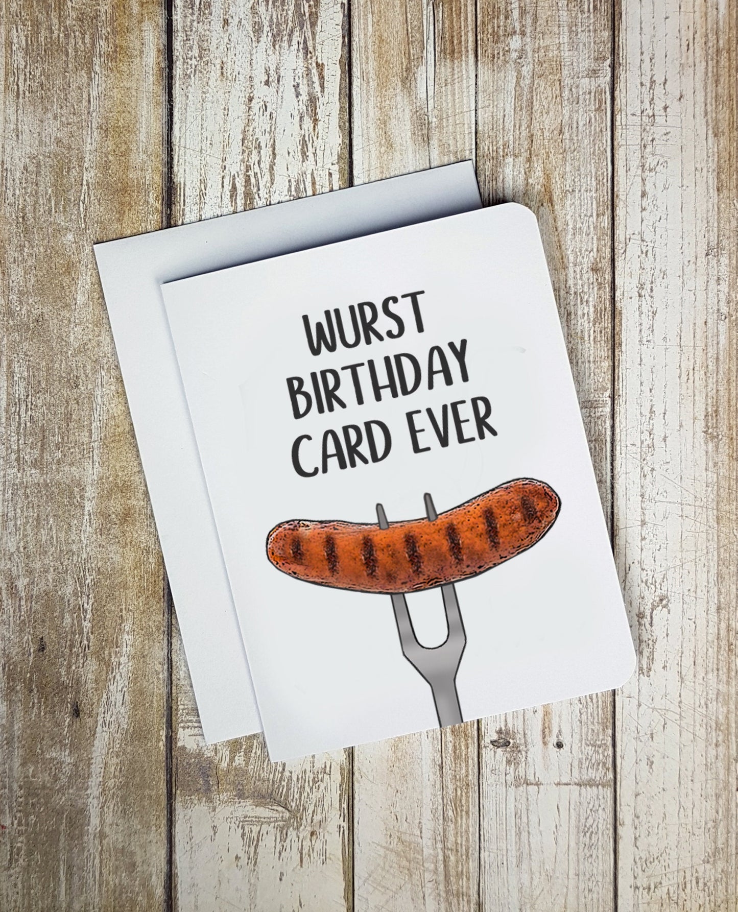 A photo of a white birthday card. It has an illustration of a sausage on a fork on it. Text on card reads, 'Wurst Birthday Card Ever.'