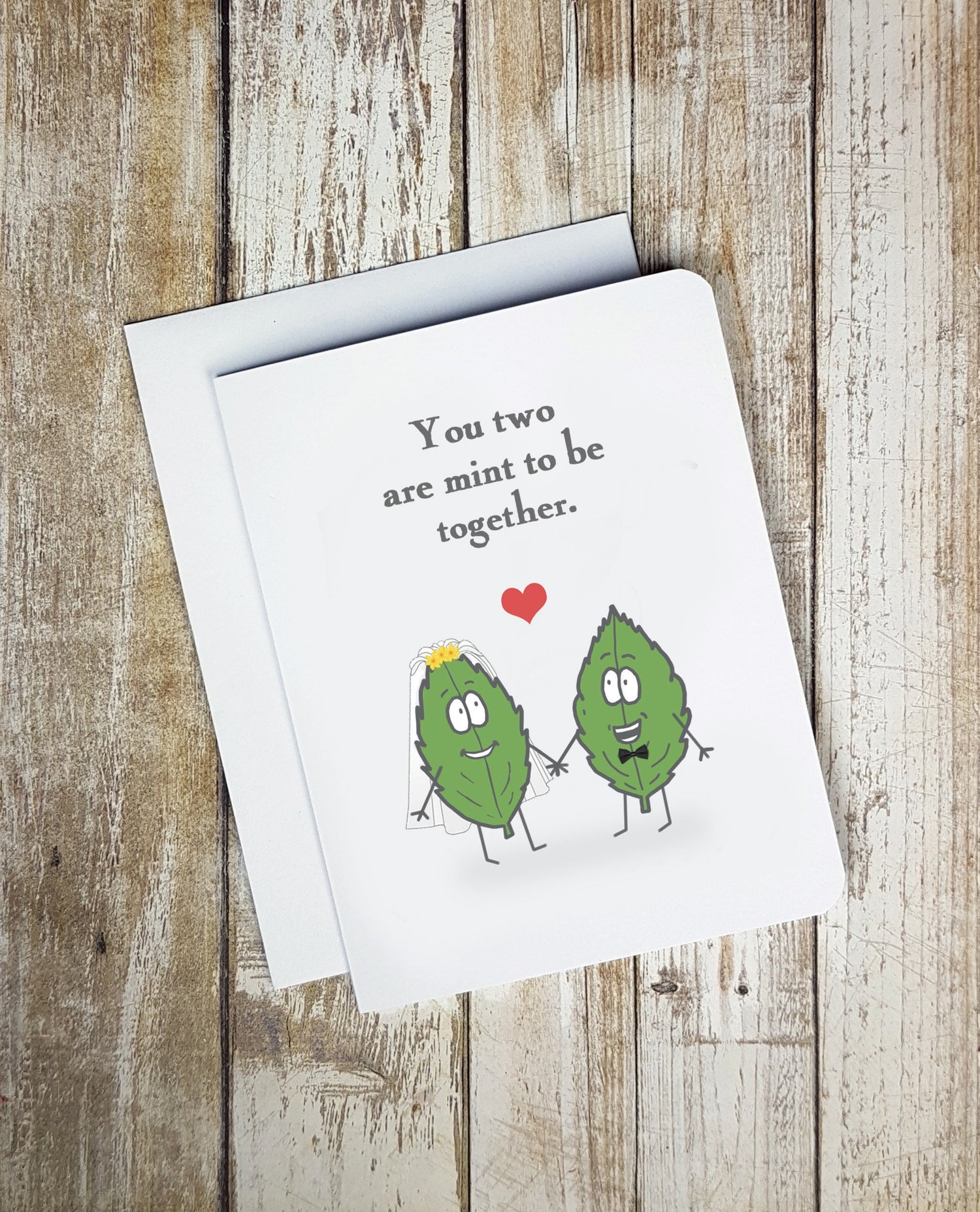 A photo of a greeting card. It has two cartoon mint leaves on it. One has a veil on, the other, a bowtie. Text reads, 'You two are mint to be together.'