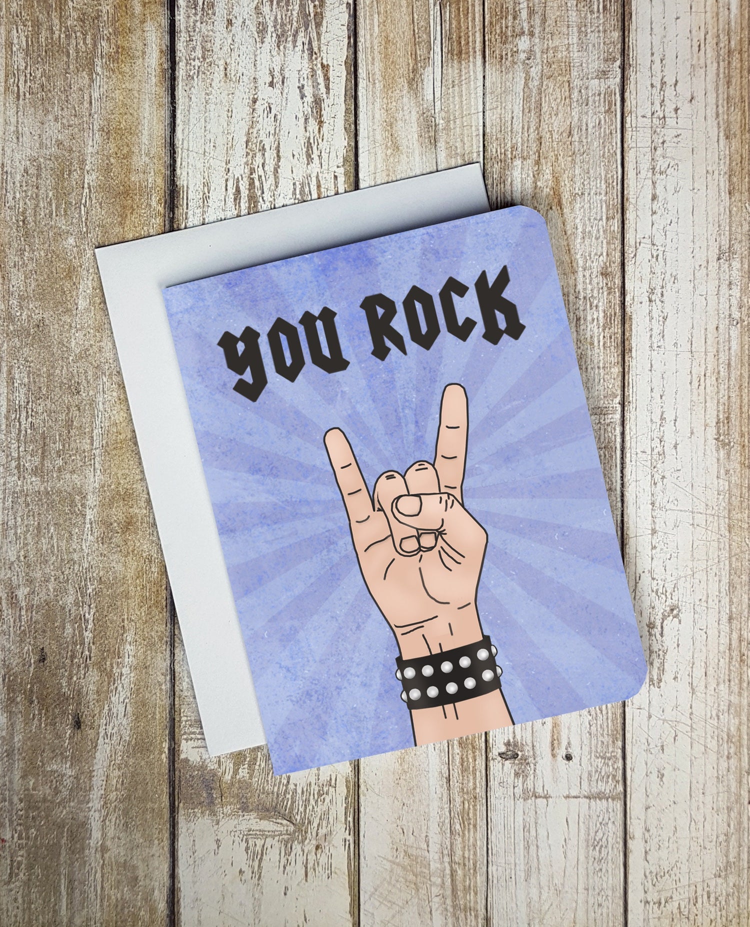 A photo of a card. It has a cartoon hand doing the rock symbol. It's wearing a studded bracelet. Text on card reads 'You Rock.'