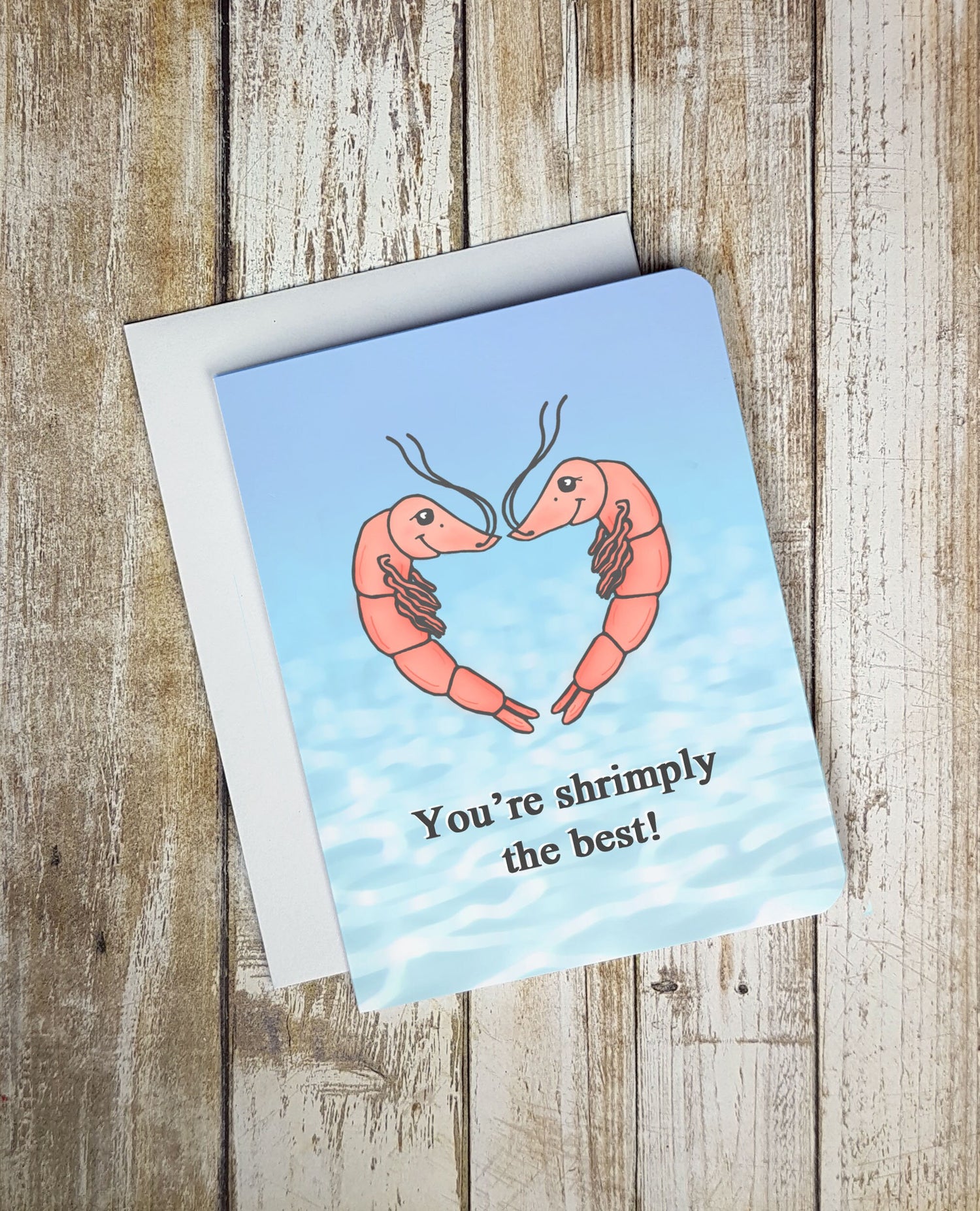 A cute Valentine's Day card. It is blue and has two shrimp on it smiling at one another in a heart shaped formation. Text blow on card reads: 'You're shrimply the best.'