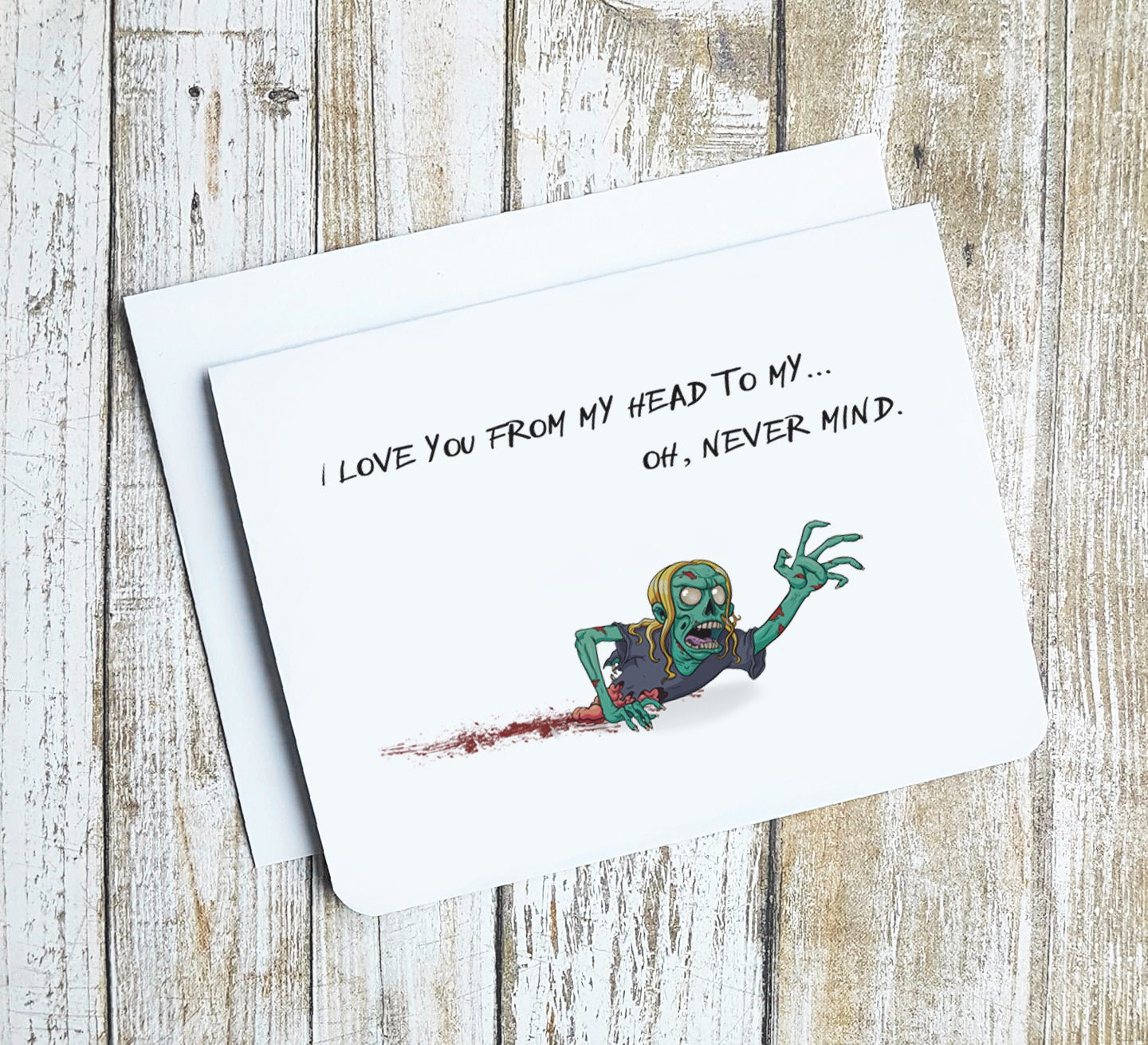 A photo of a white valentine's card. It has a crawling zombie on it. It's missing half of its body. Text on card reads, 'I love you from my head to my ... oh, never mind.'