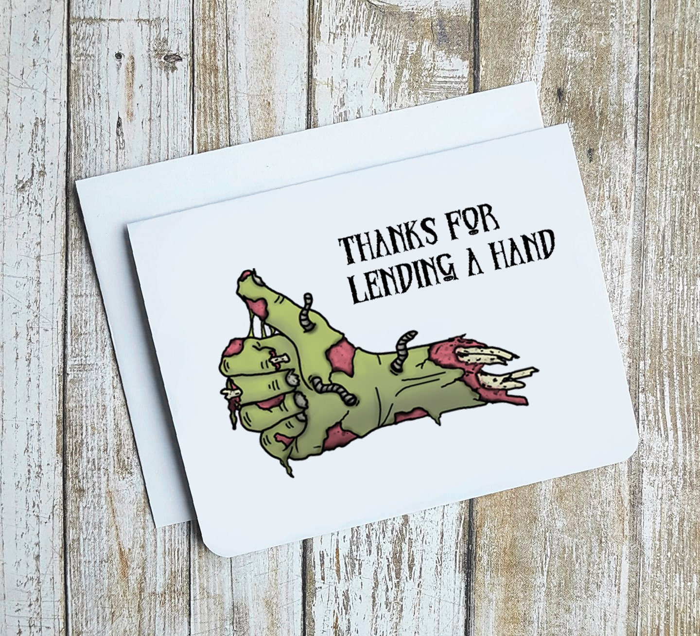 A photo of a thank you card. It has a green cartoon zombie hand on it giving the thumbs up. Text on card reads, 'Thanks for lending a hand.'