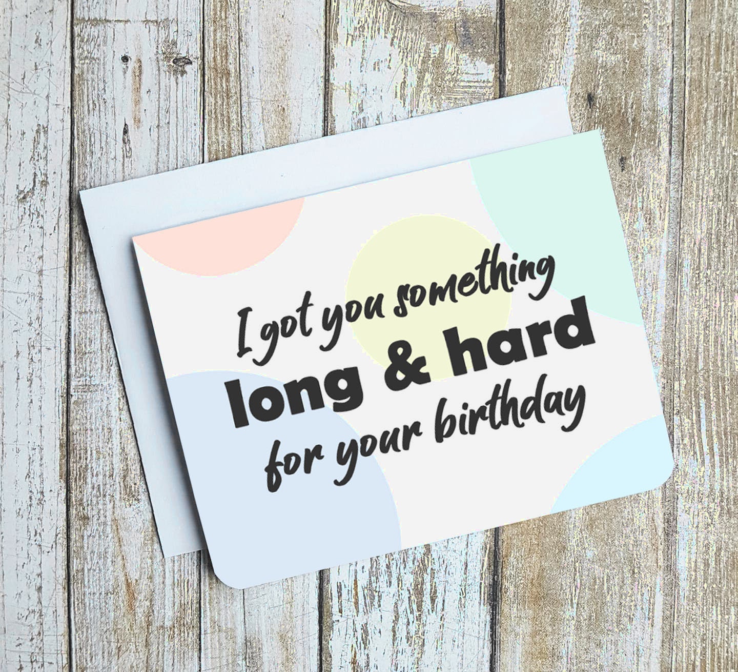 A photo of a birthday card. It has circles of pastel colours in the background. Text on card says, I got you something long & hard for your birthday.'