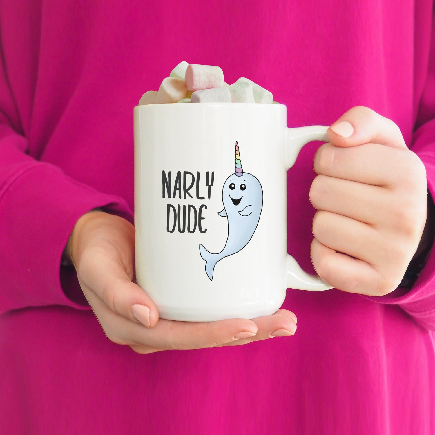 A photo of a cute mug. it has a cartoon narwhal on it with a colourful striped horn. Text reads Narly Dude.