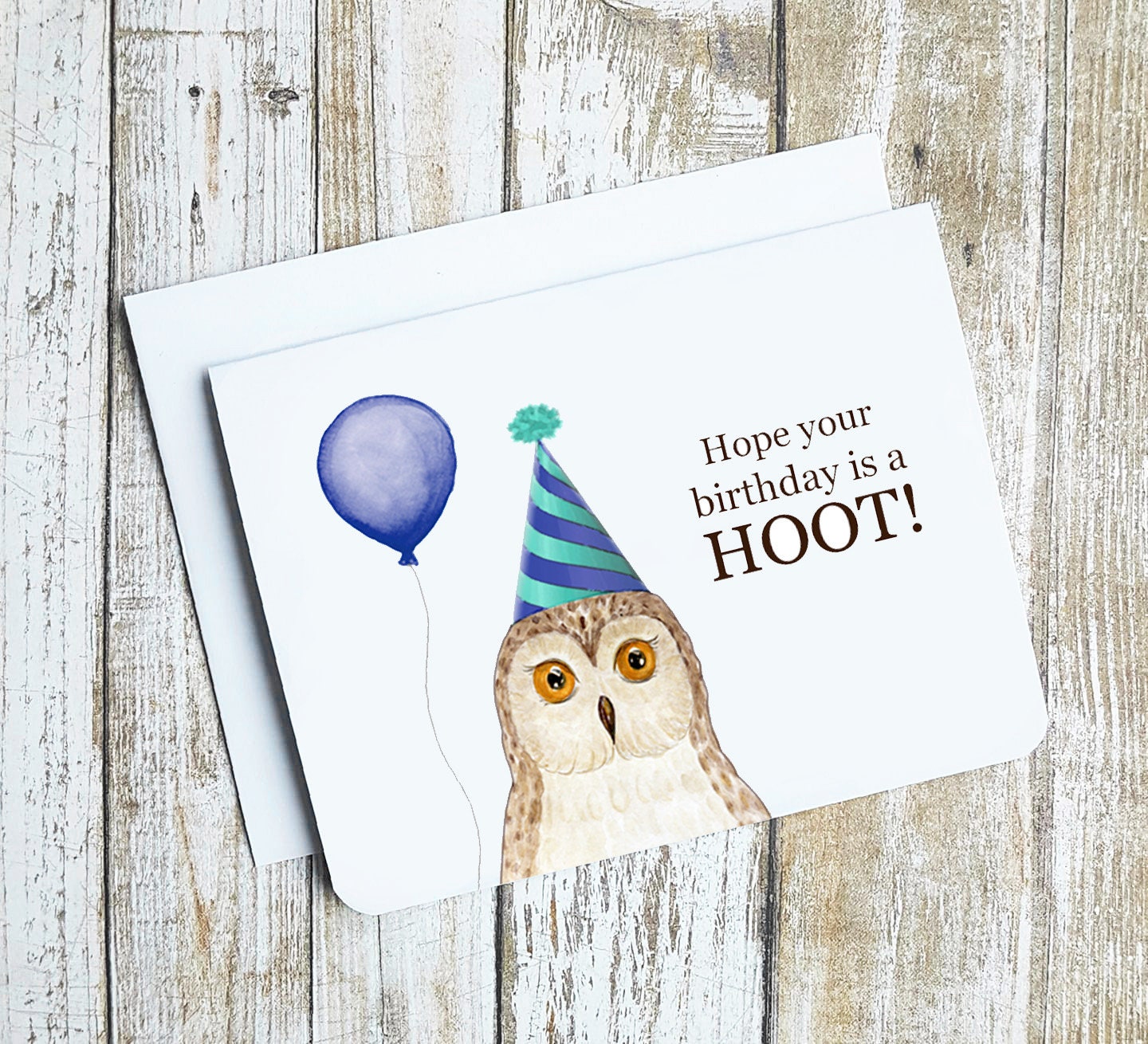 A photo of a white birthday card. It has an illustrated owl on it. It's wearing a party hat and holding a balloon. Text on card reads, Hope your birthday is a hoot!