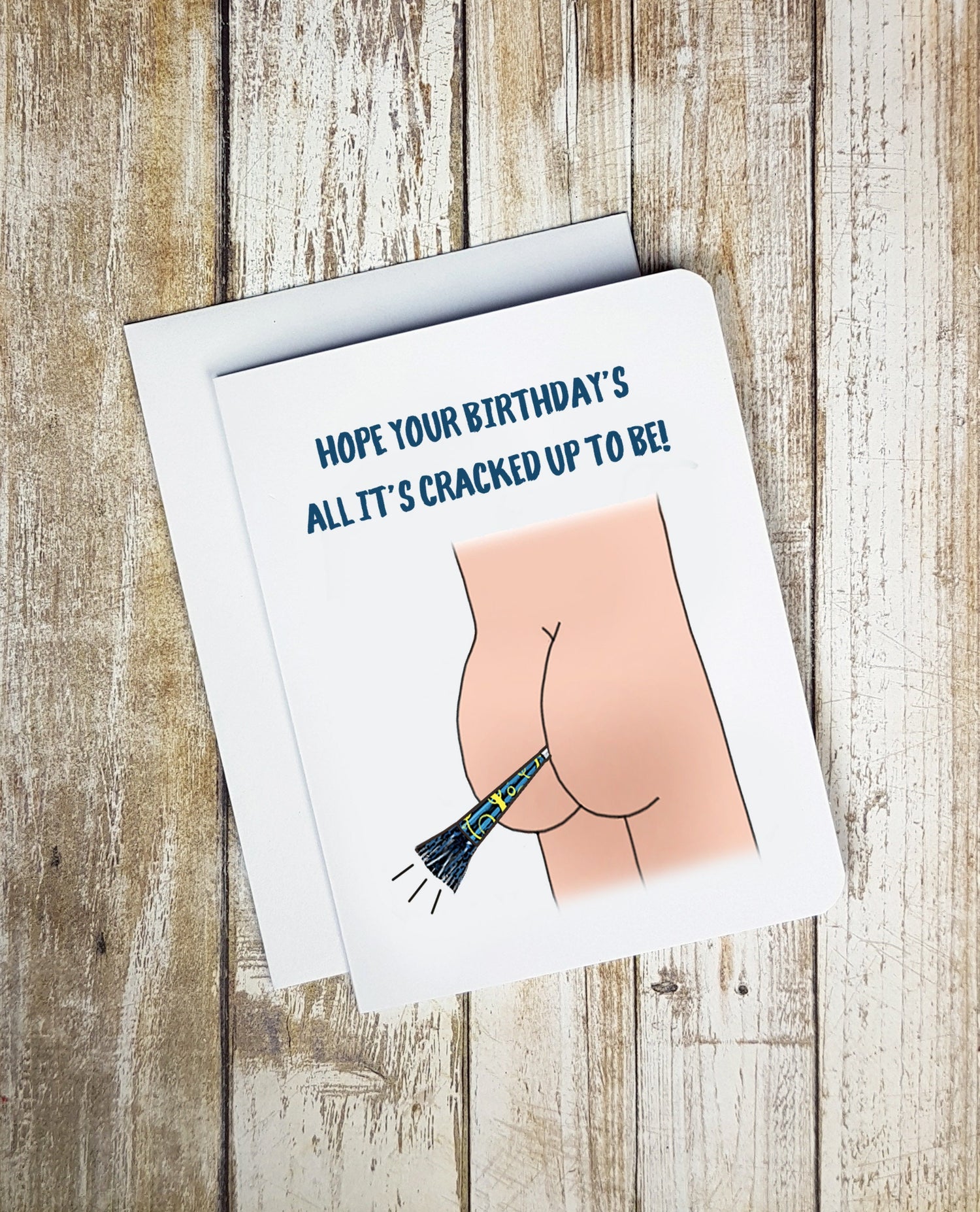 A photo of a white birthday card. It has cartoon butt cheeks on it. Between the cheeks is a party horn. Text on card reads, 'Hope Your Birthday's All It's Cracked Up to Be!'