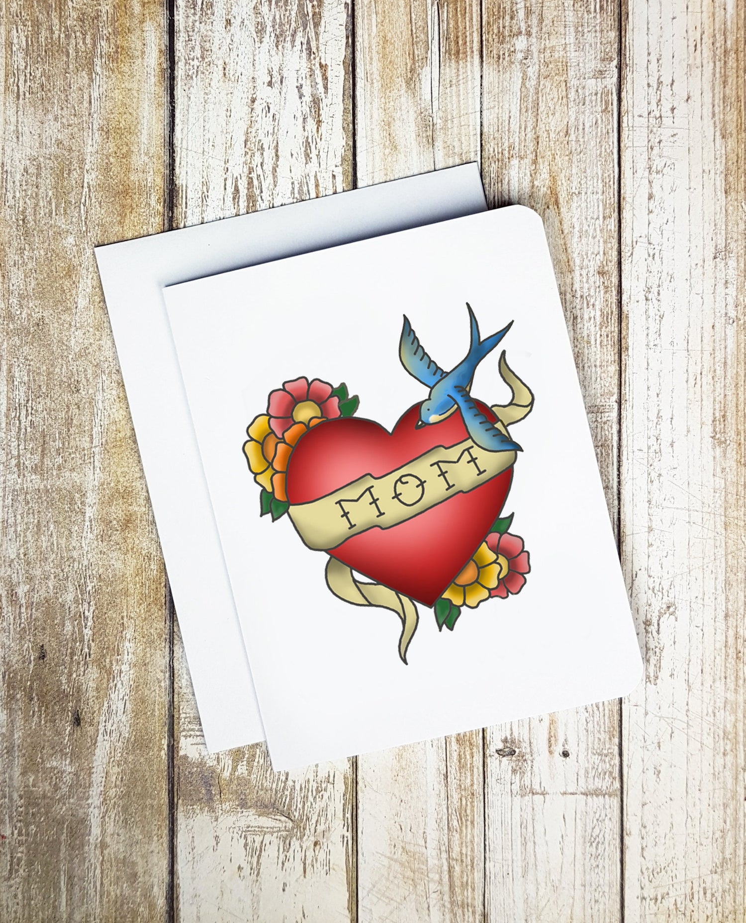 A photo of a Mother's Day card. It has a heart shaped tattoo on it with a swallow. Text on tattoo reads, MOM.