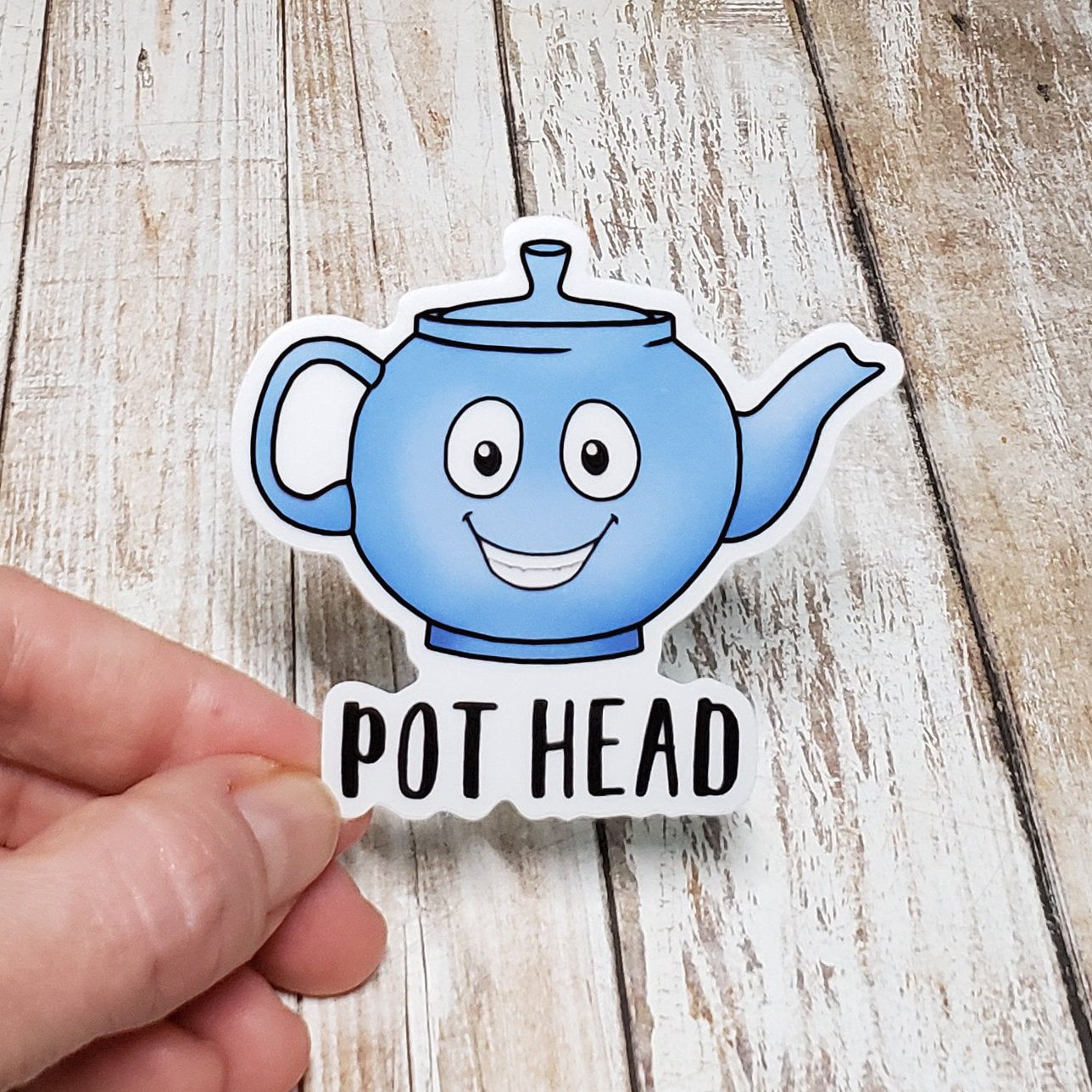 A photo of a vinyl sticker. It's of a blue cartoon tea pot which is smiling. Text on sticker reads 'Pot Head.'