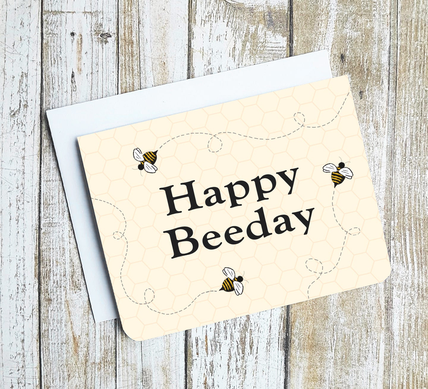 A photo of a birthday card. It has cartoon bees buzzing around on it. Text in the centre of the card reads, 'Happy Beeday.'
