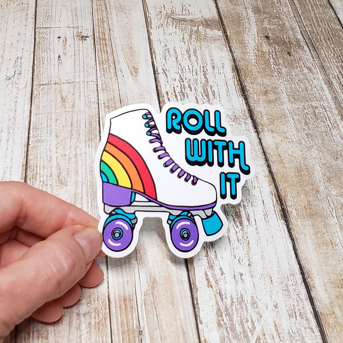 A photo of a vinyl sticker of cartoon roller-skate. Text on funny sticker reads 'Roll With It.'
