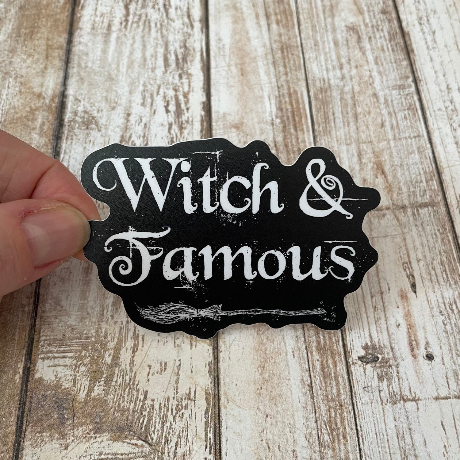 A photo of a black sticker. It has white text on it that reads 'Witch & Famous.'