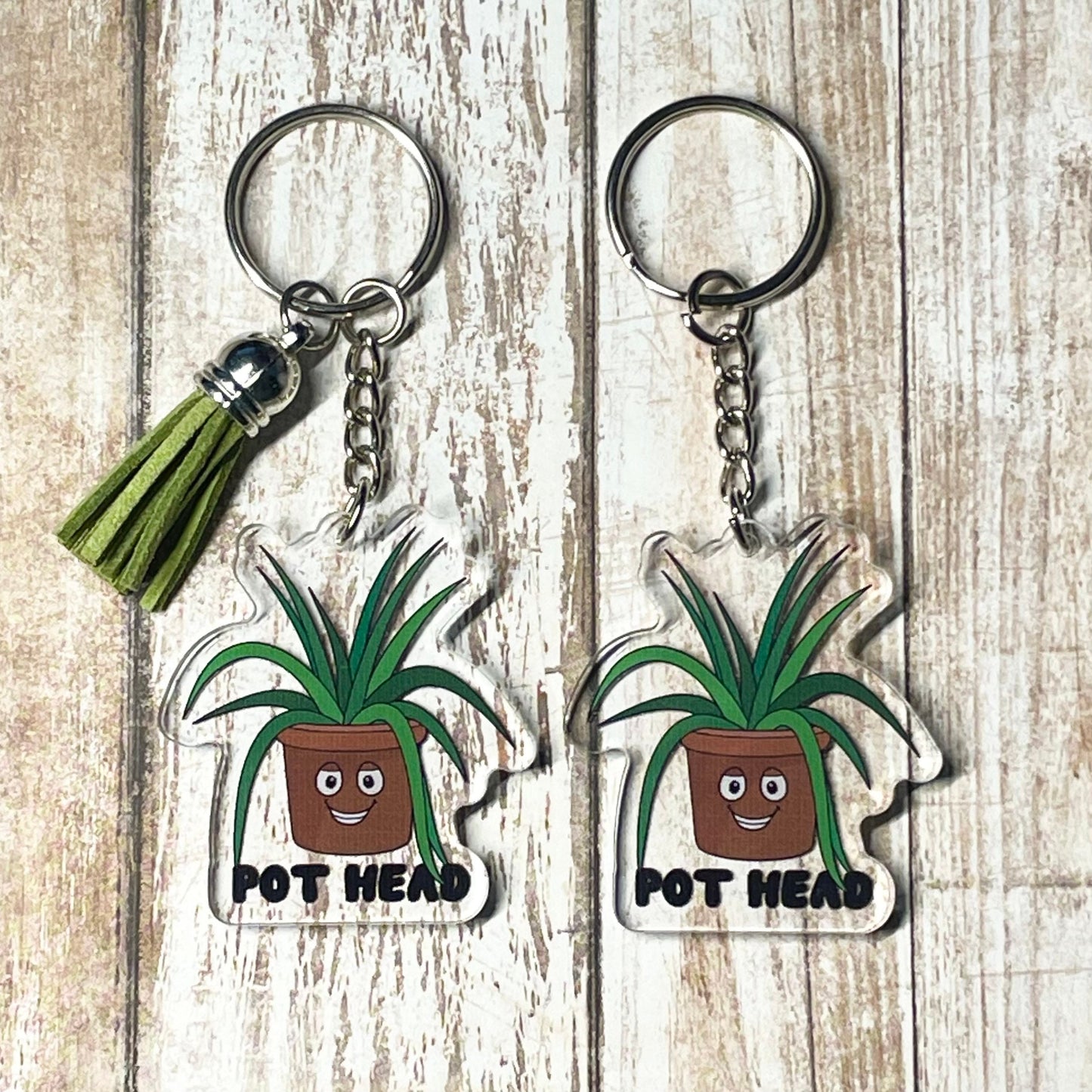 A photo of two acrylic key chains. They have smiling cartoon plant pots on them. Text on keychain reads 'Pot Head.'