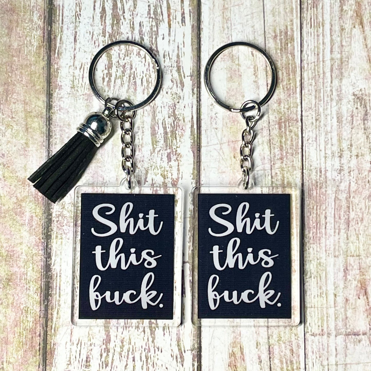 A photo of two black rectangular key chains. Text on keychains reads 'Shit this Fuck.' 